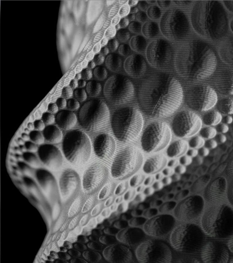 May include: Abstract grayscale sculpture with a textured surface. The design features a repeating pattern of rounded shapes, creating a dynamic and visually engaging form. The piece has a modern aesthetic and is set against a black background.