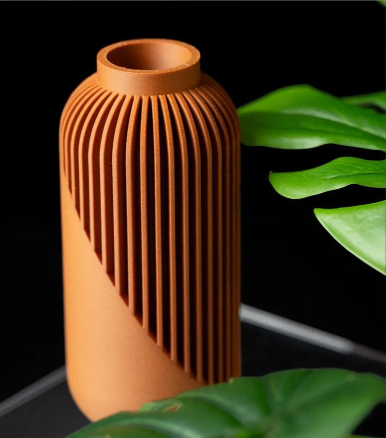 Peut inclure: Un vase de couleur terre cuite avec un corps cylindrique et un col &eacute;troit. Le vase pr&eacute;sente des d&eacute;tails verticaux et stri&eacute;s sur la partie sup&eacute;rieure, cr&eacute;ant un effet textur&eacute;. Le design comprend une coupe diagonale. Le fond est noir.