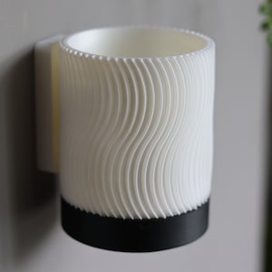 May include: White wall-mounted mug holder with a wavy textured design and a black base.