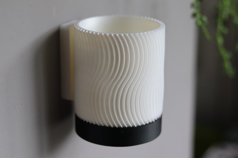 May include: White wall-mounted mug holder with a wavy textured design and a black base.