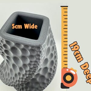 May include: A gray, textured vase with a unique, bubble-like pattern. The square opening is 2 inches wide, and the vase is 7.5 inches deep. The design is a modern, artistic take on a decorative container.