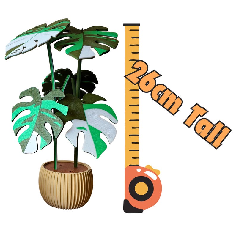 May include: A decorative plant in a gold-colored pot with large, split leaves in shades of green and white. The plant is 26cm (10.2 inches) tall, as indicated by a measuring tape graphic. The text "26cm Tall" is also present.