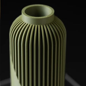 Peut inclure: Un vase vert avec un design nervur&eacute;. Le vase a une forme cylindrique avec des rainures verticales qui cr&eacute;ent une surface textur&eacute;e. Le haut du vase a une ouverture circulaire.
