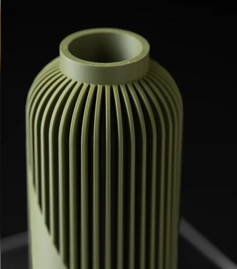 Peut inclure: Un vase vert avec un design nervur&eacute;. Le vase a une forme cylindrique avec des rainures verticales qui cr&eacute;ent une surface textur&eacute;e. Le haut du vase a une ouverture circulaire.