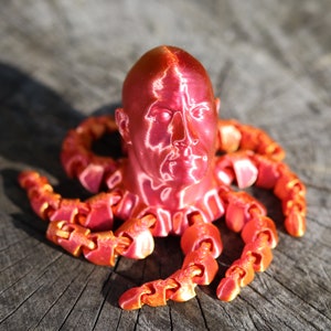 May include: A red 3D printed sculpture of a human head with octopus tentacles. The head has a detailed face and the tentacles are segmented.