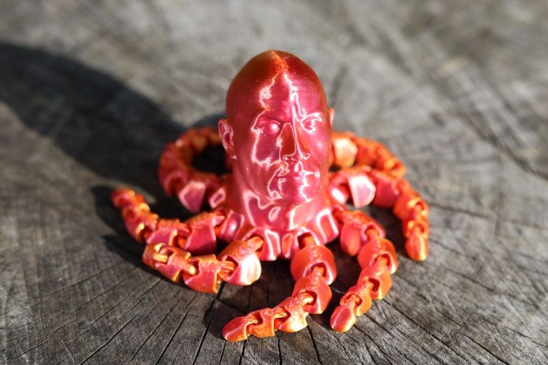 May include: A red 3D printed sculpture of a human head with octopus tentacles. The head has a detailed face and the tentacles are segmented.