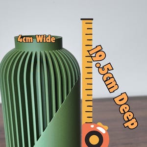 Peut inclure: Un vase vert nervur&eacute;, de 4 cm de large et 19,5 cm de profondeur, est pr&eacute;sent&eacute; &agrave; c&ocirc;t&eacute; d'un m&egrave;tre ruban. Le vase pr&eacute;sente un design textur&eacute; unique. L'image est bien &eacute;clair&eacute;e, mettant en valeur les d&eacute;tails du vase et les &eacute;tiquettes de mesure.