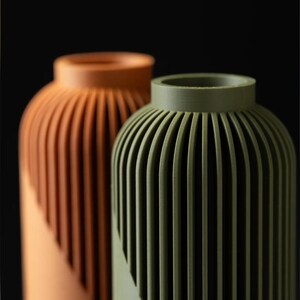 Peut inclure: Deux vases d&eacute;coratifs avec un design c&ocirc;tel&eacute;. L'un est de couleur terre cuite chaude, l'autre vert olive. Les vases ont une forme cylindrique avec un dessus arrondi et un motif diagonal sur la moiti&eacute; inf&eacute;rieure.