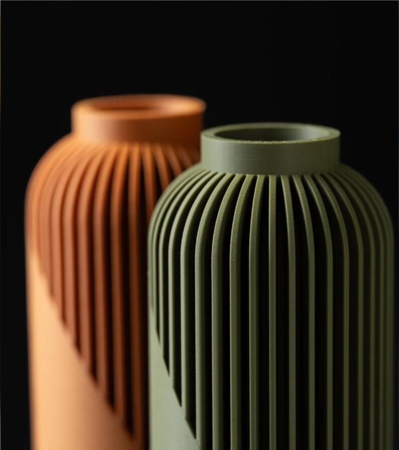 Peut inclure: Deux vases d&eacute;coratifs avec un design c&ocirc;tel&eacute;. L'un est de couleur terre cuite chaude, l'autre vert olive. Les vases ont une forme cylindrique avec un dessus arrondi et un motif diagonal sur la moiti&eacute; inf&eacute;rieure.