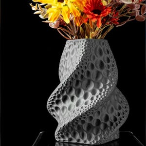 May include: A gray, textured vase with a spiral design, filled with colorful artificial flowers. The vase has a unique pattern of raised circles and a twisted shape. The flowers include yellow, orange, and red blooms.