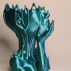 May include: A teal blue 3D printed sculpture of a person's head and shoulders with their hands clasped together in front of their face. The sculpture has a flowing, organic design.
