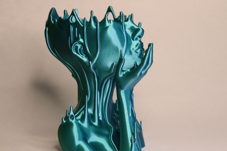 May include: A teal blue 3D printed sculpture of a person's head and shoulders with their hands clasped together in front of their face. The sculpture has a flowing, organic design.