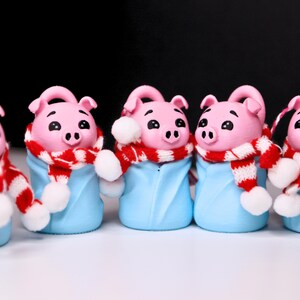May include: Five pink pig figurines wearing blue and white pajamas with red and white striped scarves. The pig figurines are wearing white pom-poms on their scarves.