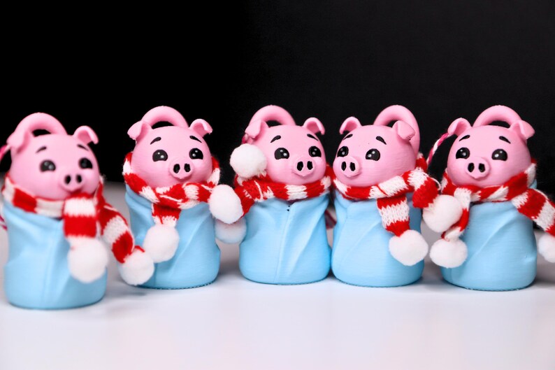 May include: Five pink pig figurines wearing blue and white pajamas with red and white striped scarves. The pig figurines are wearing white pom-poms on their scarves.