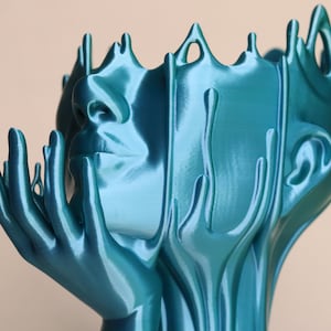 May include: A teal blue abstract sculpture of a face with hands reaching up. The sculpture is made of a smooth, flowing material that resembles liquid.