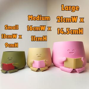 Puede incluir: Tres macetas de cer&aacute;mica de colores con forma de personajes de dibujos animados leyendo libros. Las macetas son de tres tama&ntilde;os: peque&ntilde;a (13 cm de ancho x 9 cm de alto), mediana (16 cm de ancho x 11 cm de alto) y grande (21 cm de ancho x 14,5 cm de alto).