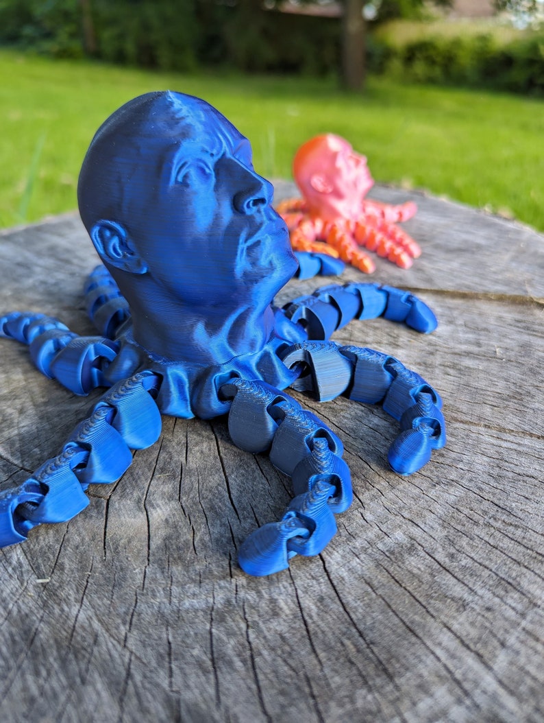 May include: A blue 3D printed octopus with a human face. The octopus has eight tentacles and is sitting on a wooden surface.