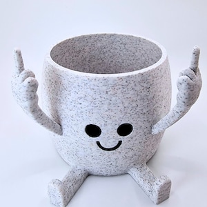 May include: White ceramic planter with a speckled finish, shaped like a person with two arms raised in the air and two legs. The planter has a smiling face with two black eyes.