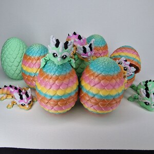 Puede incluir: Un grupo de huevos de drag&oacute;n coloridos con algunos dragones saliendo de ellos. Los huevos est&aacute;n decorados con un patr&oacute;n de escamas y tienen un esquema de colores arco&iacute;ris. Los dragones son peque&ntilde;os y tienen colores verde, rosa y blanco.