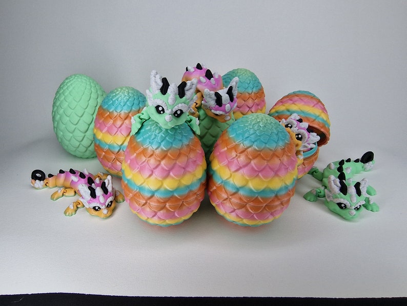 Puede incluir: Un grupo de huevos de drag&oacute;n coloridos con algunos dragones saliendo de ellos. Los huevos est&aacute;n decorados con un patr&oacute;n de escamas y tienen un esquema de colores arco&iacute;ris. Los dragones son peque&ntilde;os y tienen colores verde, rosa y blanco.