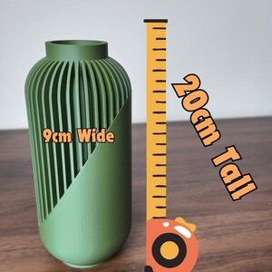 Peut inclure: Un vase vert avec un design c&ocirc;tel&eacute; unique, de 9 cm de large et 20 cm de haut. Le vase a une forme lisse et incurv&eacute;e et une coupe diagonale sur un c&ocirc;t&eacute;. Le texte "9cm Wide" et "20cm Tall" sont visibles.