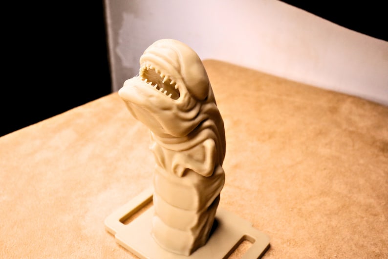 May include: A beige 3D printed figurine of a creature with a large mouth and sharp teeth. The figurine is standing on a beige base.
