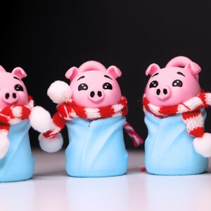 May include: Three pink pig figurines wearing blue and white winter outfits with red and white striped scarves. The pigs have black eyes and snouts.