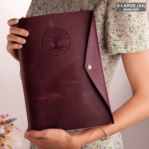 May include: Burgundy leather portfolio with a tree of life design and the text "LILY'S SKETCHES" embossed on the front.