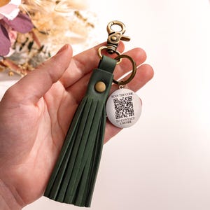 May include: A green leather tassel keychain with a silver round tag that says "SCAN THE CODE TO CONTACT OWNER" and has a black and white QR code.
