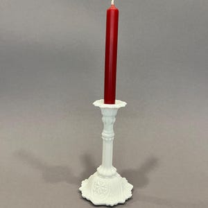 Könnte beinhalten: Weißer Kerzenständer aus Keramik mit einer roten Kerze. Der Kerzenständer hat eine dekorative Basis und einen hohen, schlanken Stiel.