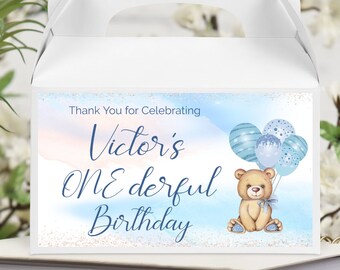 May include: Blue and white favor box with a teddy bear and balloons. The box says "Thank You for Celebrating Victor's One Derful Birthday".