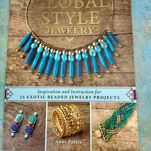 May include: A book titled "GLOBAL STYLE JEWELRY" with a gold necklace featuring blue beads. The book cover displays various beaded jewelry projects, including earrings, a ring, and a bracelet. The text reads "Inspiration and Instruction for 25 EXOTIC BEADED JEWELRY PROJECTS."
