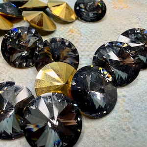 May include: Close-up of various faceted crystal rhinestones. The rhinestones are in shades of black and gold. The black rhinestones are round, while the gold ones are pointed. These decorative crystals are ideal for crafts and embellishments.