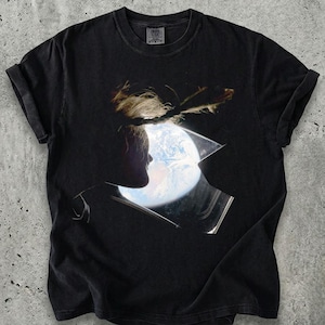 May include: A white ceramic mug with a black handle and the text "But First, Coffee" in a bold, black font. The mug is set against a blurred background, suggesting a cozy setting.