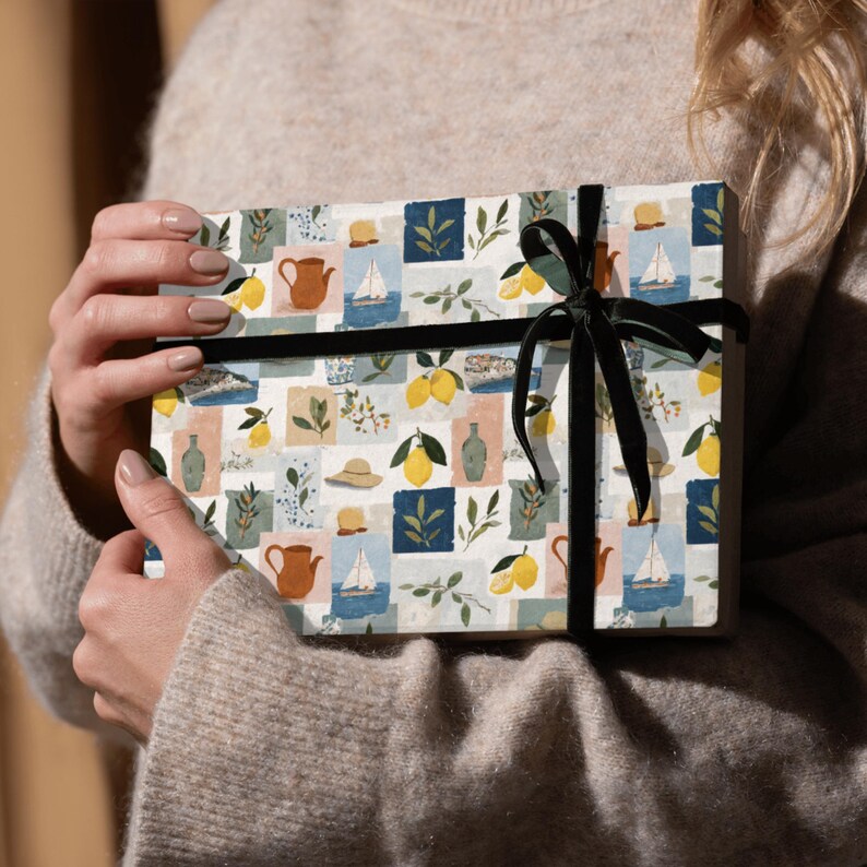 May include: A wrapped gift with a patterned paper featuring lemons, sailboats, hats, and teapots in a grid design. The gift is tied with a black velvet ribbon. The overall color scheme includes white, blue, yellow, and brown.