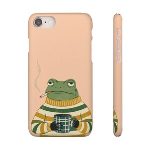 Può includere: Custodia per telefono color pesca con un'illustrazione di rana dei cartoni animati. La rana fuma una sigaretta e tiene in mano una tazza, indossando un maglione a righe verdi e gialle.