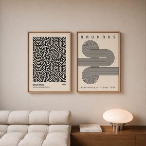 Pode incluir: Duas impressões de arte Bauhaus emolduradas. Uma apresenta um padrão abstrato em preto e branco, a outra um design geométrico em preto e branco com a palavra "Bauhaus". Ambas estão em molduras douradas.