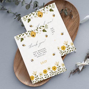 Op de afbeelding: Twee witte bedankkaarten met een bijenthema. De kaarten hebben een honingraatpatroon, gele en witte bloemen en illustraties van bijen en bijenkorven. Tekst bevat "Bedankt!" en "Om mijn verjaardag zo leuk en speciaal te maken!"
