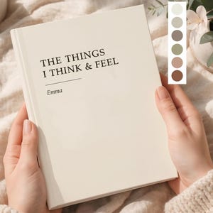 May include: A cream-colored journal titled "THE THINGS I THINK & FEEL" with the name "Emma" below. The journal is held open, revealing the blank pages. A color palette of neutral tones is displayed on the right.