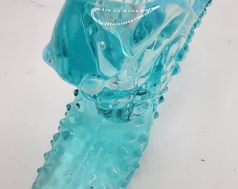 May include: A light blue glass foot roller with a textured surface. The roller is shaped like a foot and has a pointed toe.