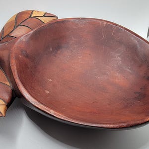 May include: A wooden bowl shaped like a leaf with a dark brown finish. The bowl has a carved leaf design on the side.