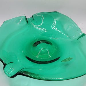 Può includere: Una ciotola di vetro verde con un bordo ondulato e arricciato. La ciotola ha un centro leggermente rialzato e una finitura liscia e lucida.