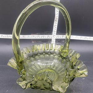 May include: A green glass basket with a ruffled edge and a handle. The basket is made of clear glass with a green tint.