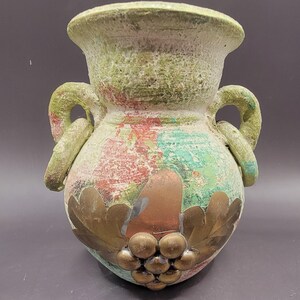 May include: A green ceramic vase with two handles and a distressed finish. The vase has a design of gold leaves and grapes on the front.
