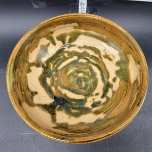 Op de afbeelding: Een keramische kom met een bruine glazuur en een swirlend groen en blauw ontwerp.