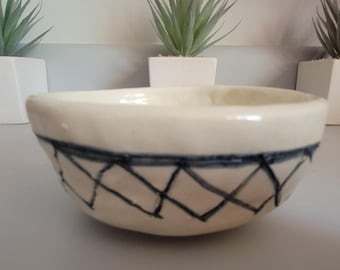 May include: A white ceramic bowl with a black and white geometric design. The bowl has a rounded shape and a slightly flared rim.