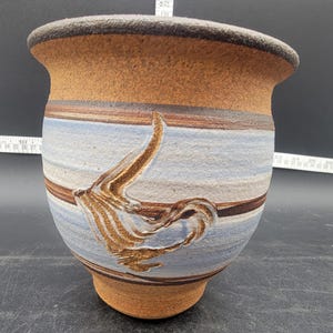 May include: A brown ceramic planter with a blue and white striped design and a brown stylized bird design.
