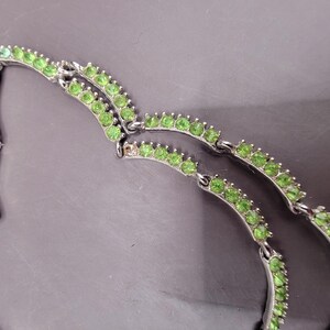 May include: A silver necklace with two rows of green stones. The stones are set in a silver metal frame.