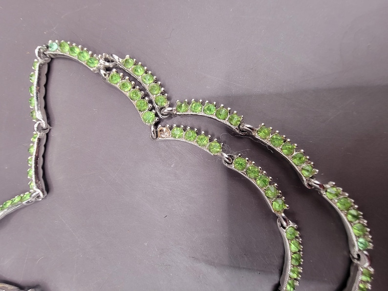 May include: A silver necklace with two rows of green stones. The stones are set in a silver metal frame.