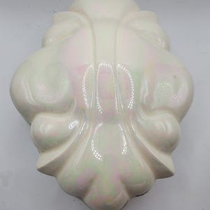 Peut inclure: Un porte-objets mural en céramique blanche avec un glaçage iridescent. Le porte-objets a un bord festonné et un motif floral.